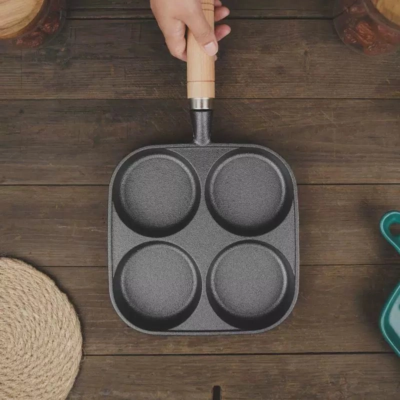 4-cup cast iron egg pan with wooden handle held in hand for scale displayed on wooden tabletop KL-KA-GAD-002