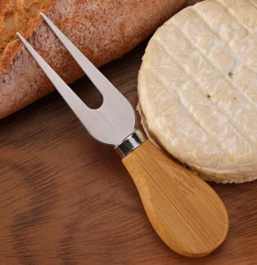 2-tine stainless steel cheese fork with wooden handle next to brie and bread displayed on wooden tabletop, KL-KA-GAD-007.