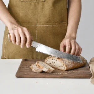 Damascus serrated bread knife being used to slice bread on a cutting board in kitchen environment KL-KN-DS-022