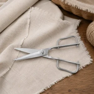 Stainless steel garden scissors resting on linen fabric and a wooden table. KL-SC-PR-002-03