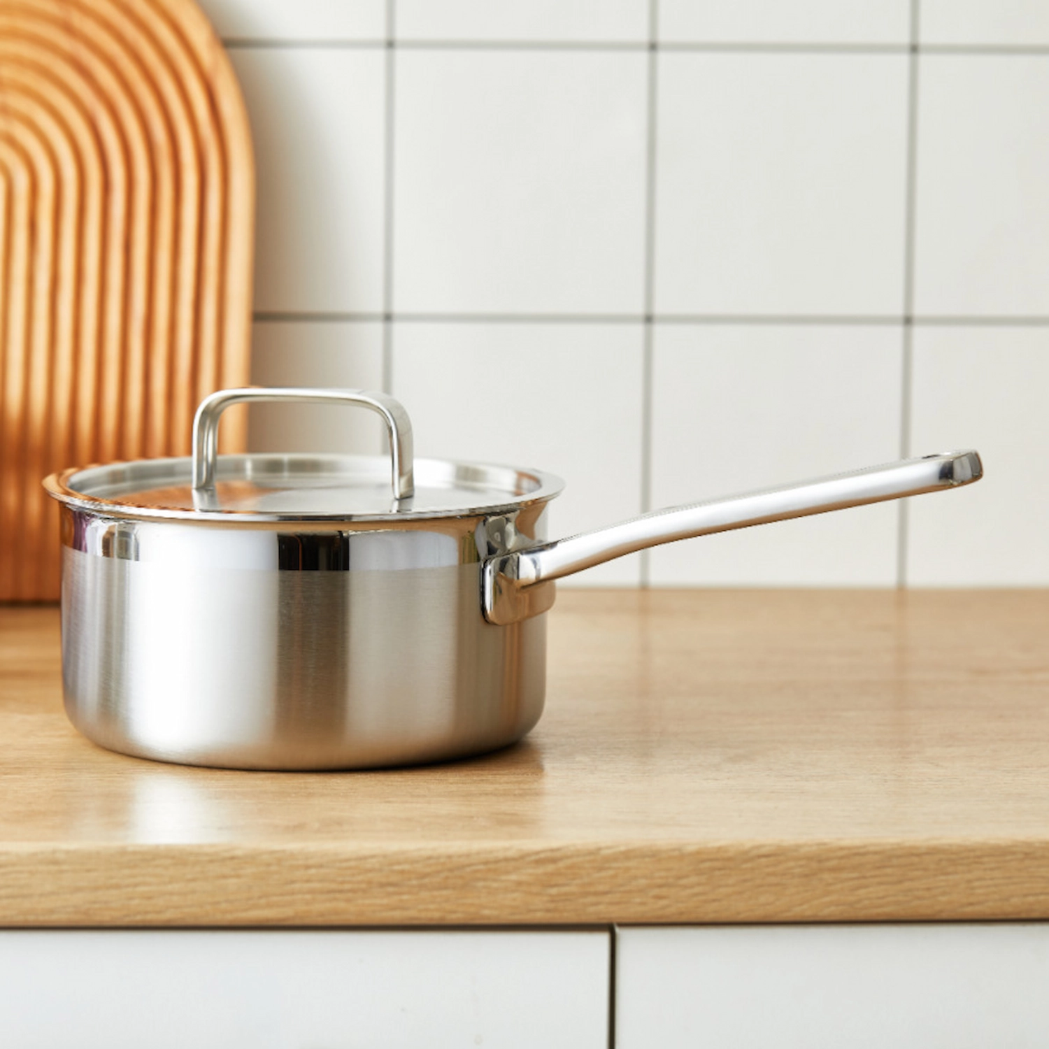 Stainless steel saucepan with lid and long handle displayed on wooden tabletop in kitchen environment KL-KA-CU-002